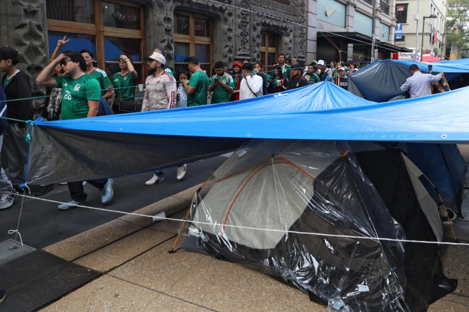 Người hâm mộ đi ngang qua khu lều trại biểu tình khi tiến về lối vào khu vực fan zone ở Mexico City trước trận đấu bảng A World Cup 2026 giữa Mexico và Nam Phi ngày 11/6. Ảnh: AFP